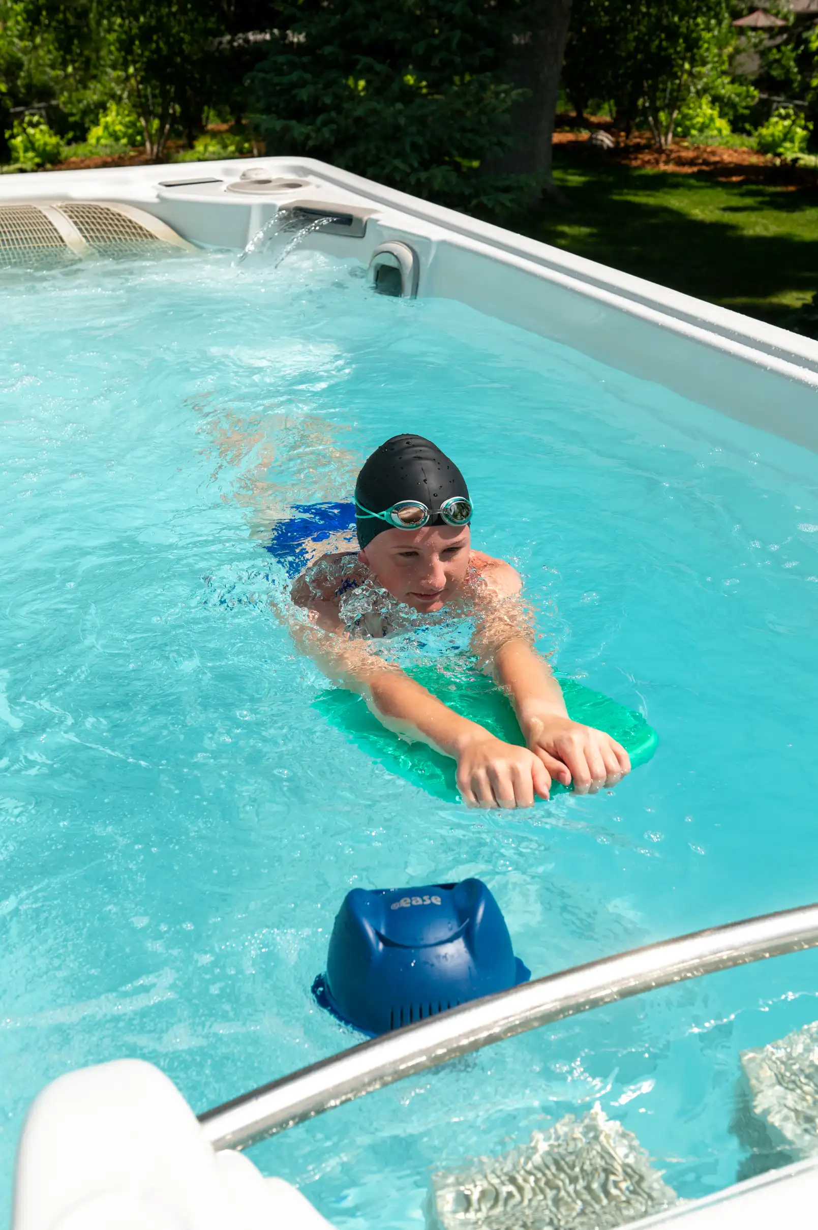 Person swimming with kickboard in swim spa, blue FROG @ease Floating System.