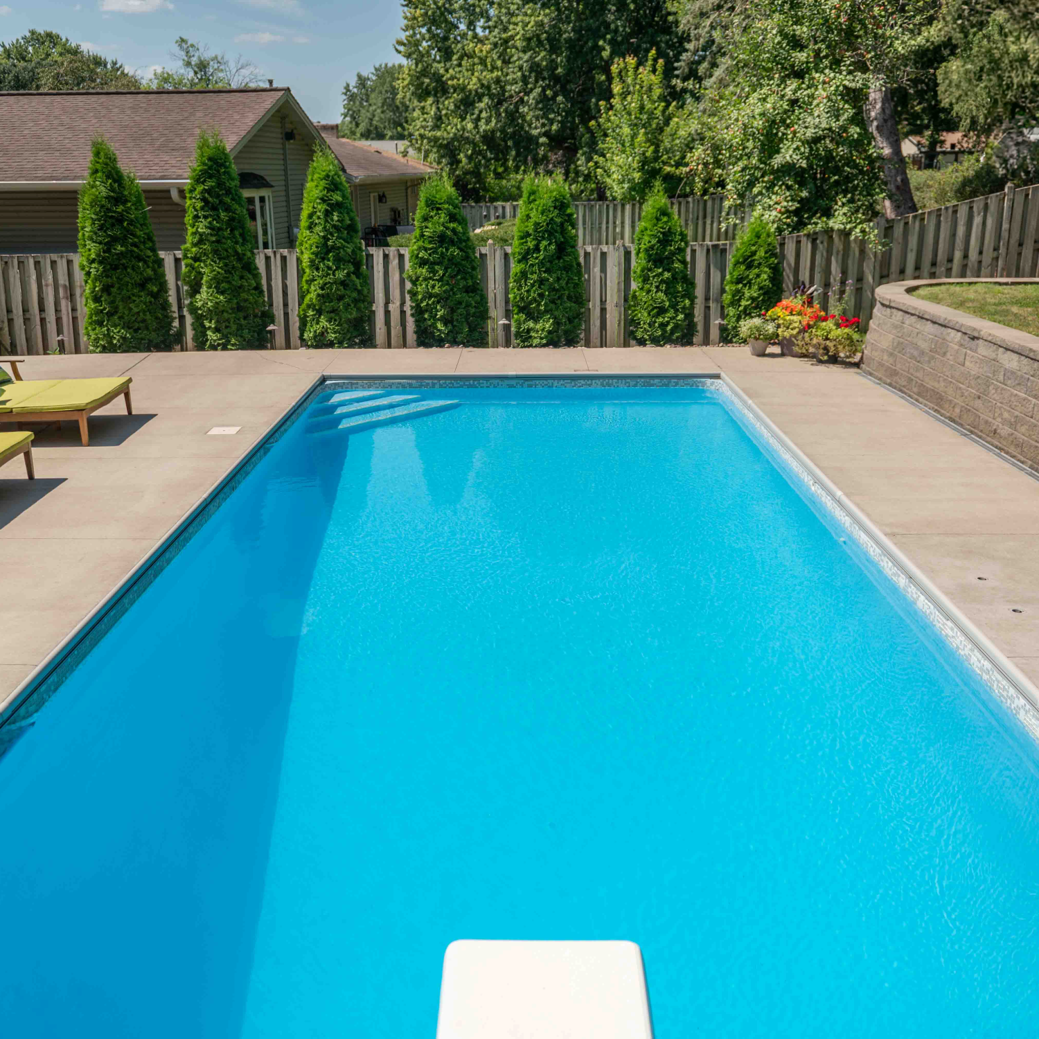 Backyard swimming pool with clear blue water, diving board, and lounge chairs on a sunny day